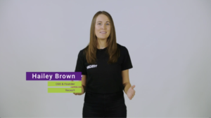 Hailey wears black Vacayit shirt shirt and stands in white studio setting. Heris title appears in purple and green box in lower-left corner 'Hailey Brown, Founder Vacayit'