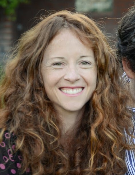 Headshot of Zara smiling with long curly red hair and fair skin.