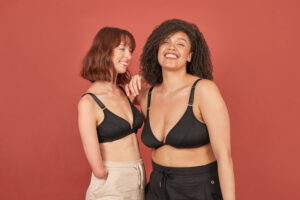 Two young, beautiful women wearing a Springrose front closure bra in black. Both women are smiling wide looking joyful.