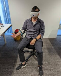 Raphael from Virtetic sitting in a chair wearing a virtual reality headset and a Virtetic sensor on his arm.