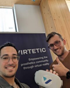 Ricardo and Raphael from Virtetic standing in front of a Virtetic banner. Raphael is holding a virtual reality headset.