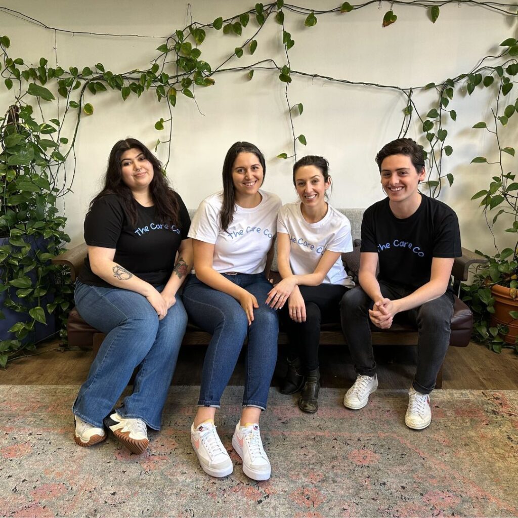 Four members from The Care Co team seated on a couch, smiling at the camera and wearing The Care Co t-shirts.