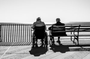 Person sat on bench facing the ocean next to person in wheelchair